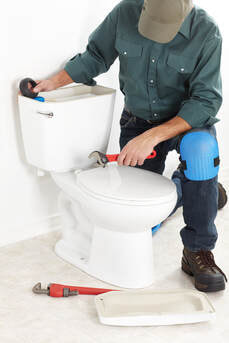 ogden plumber kneeling next to a toilet while fixing it